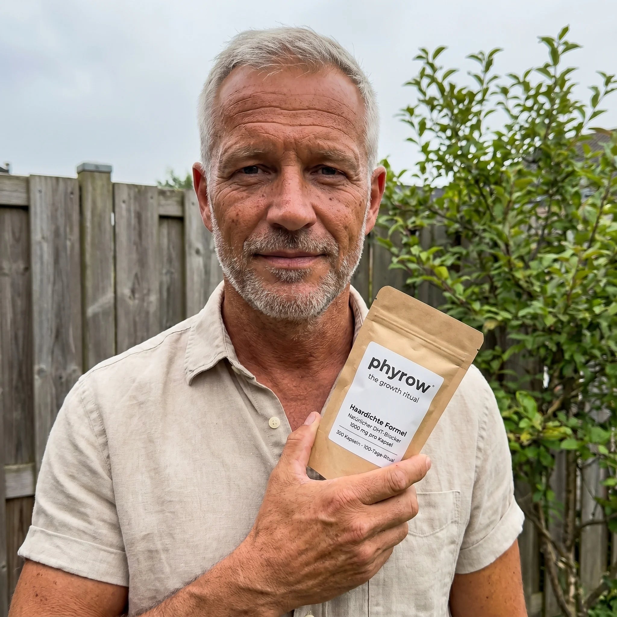 Mann Anfang 50 im Garten, beiges Leinenhemd, hält den Phyrow-Pouch lässig an der Hüfte.